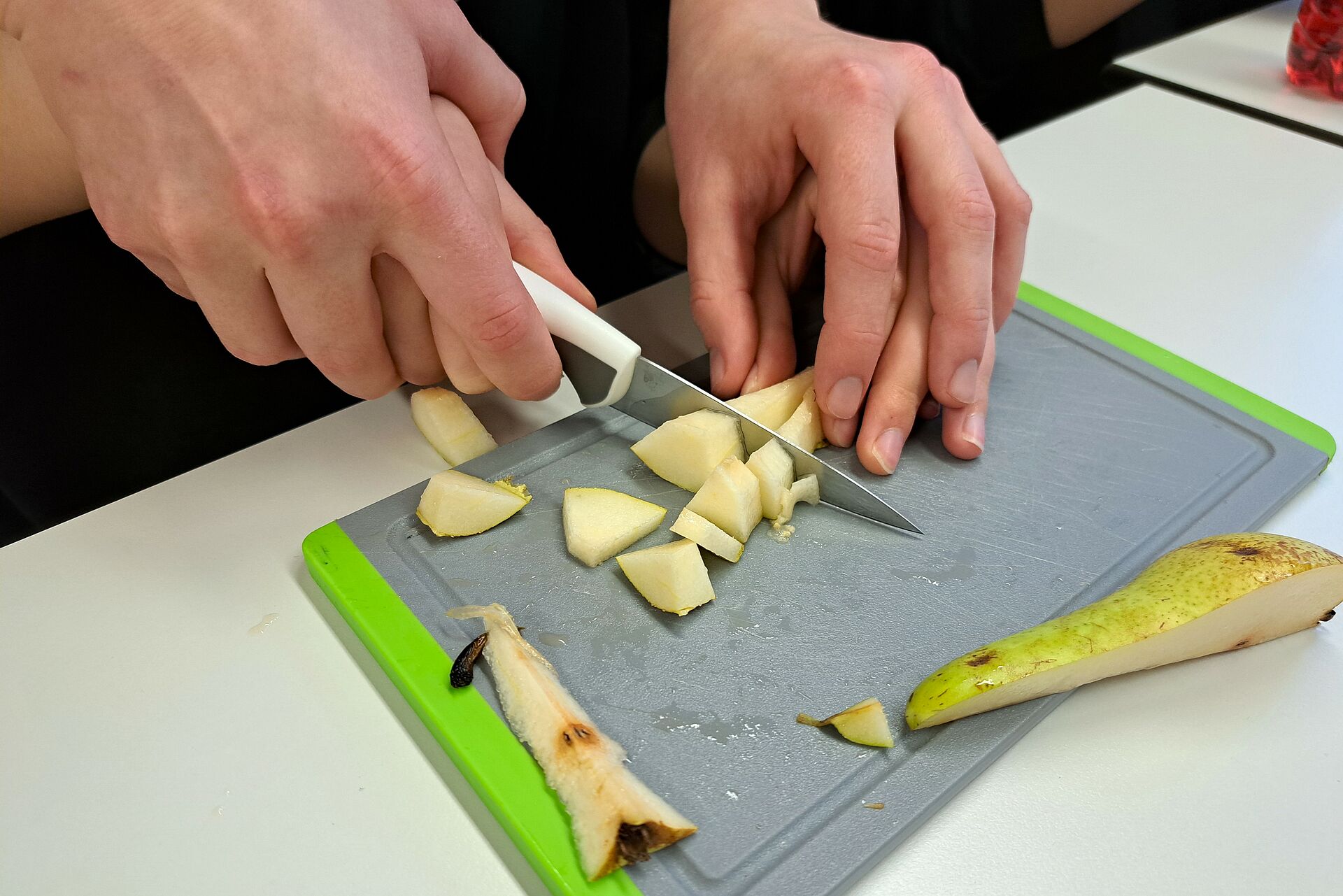 Beim Schneiden der Birne auf dem Brett wird die Hand durch eine andere Person geführt