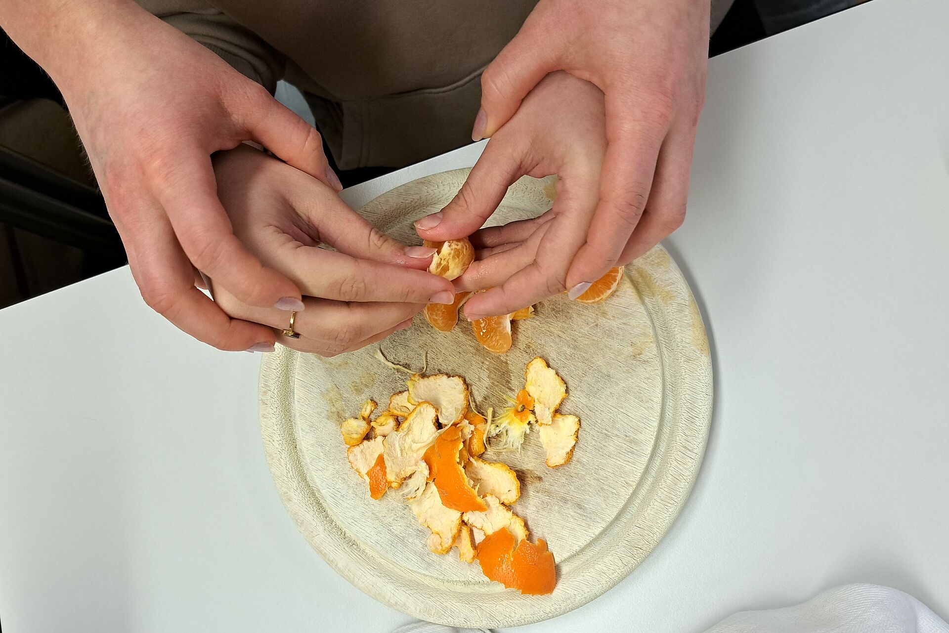 Vier Hände von zwei Personen schälen eine Mandarine. Eine Person wird dabei geführt